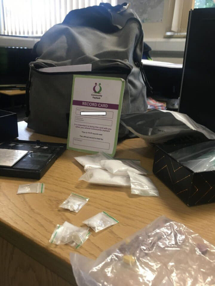 A police photo of a backpack surrounded by bags full of white power, a scale and an identity card.