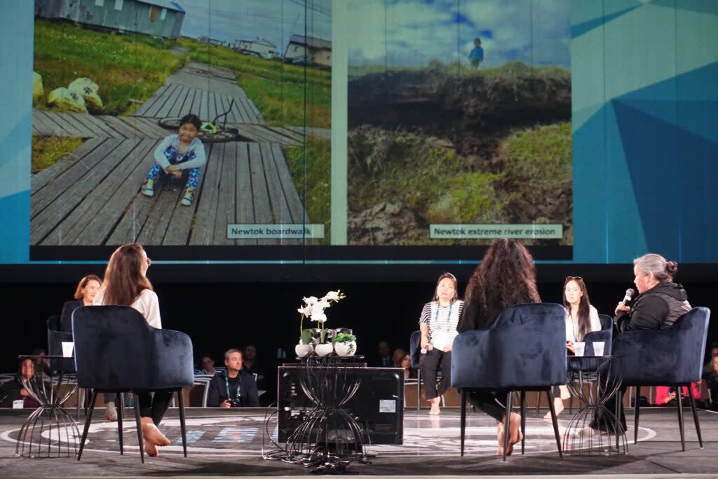 The "Newtok Mothers" assembled as a panel at the Arctic Encounter Symposium on April 11, 2024, discuss the progress and challenges as village residents move from the eroding and thawing old site to a new village site called Mertarvik. Photographs showing deteriorating conditions in Newtok are displayed on a screen as the women speak at the event, held at Anchorage's Dena'ina Civic and Convention Center. (Photo by Yereth Rosen/Alaska Beacon)