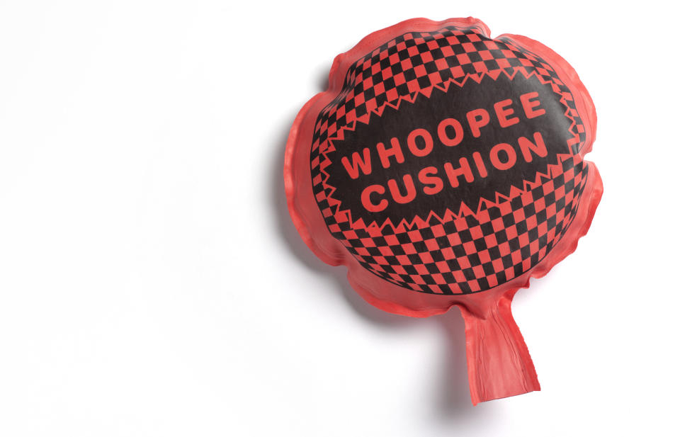 A whoopee cushion with "WHOOPEE CUSHION" text, checkered pattern on top, inflated on white background