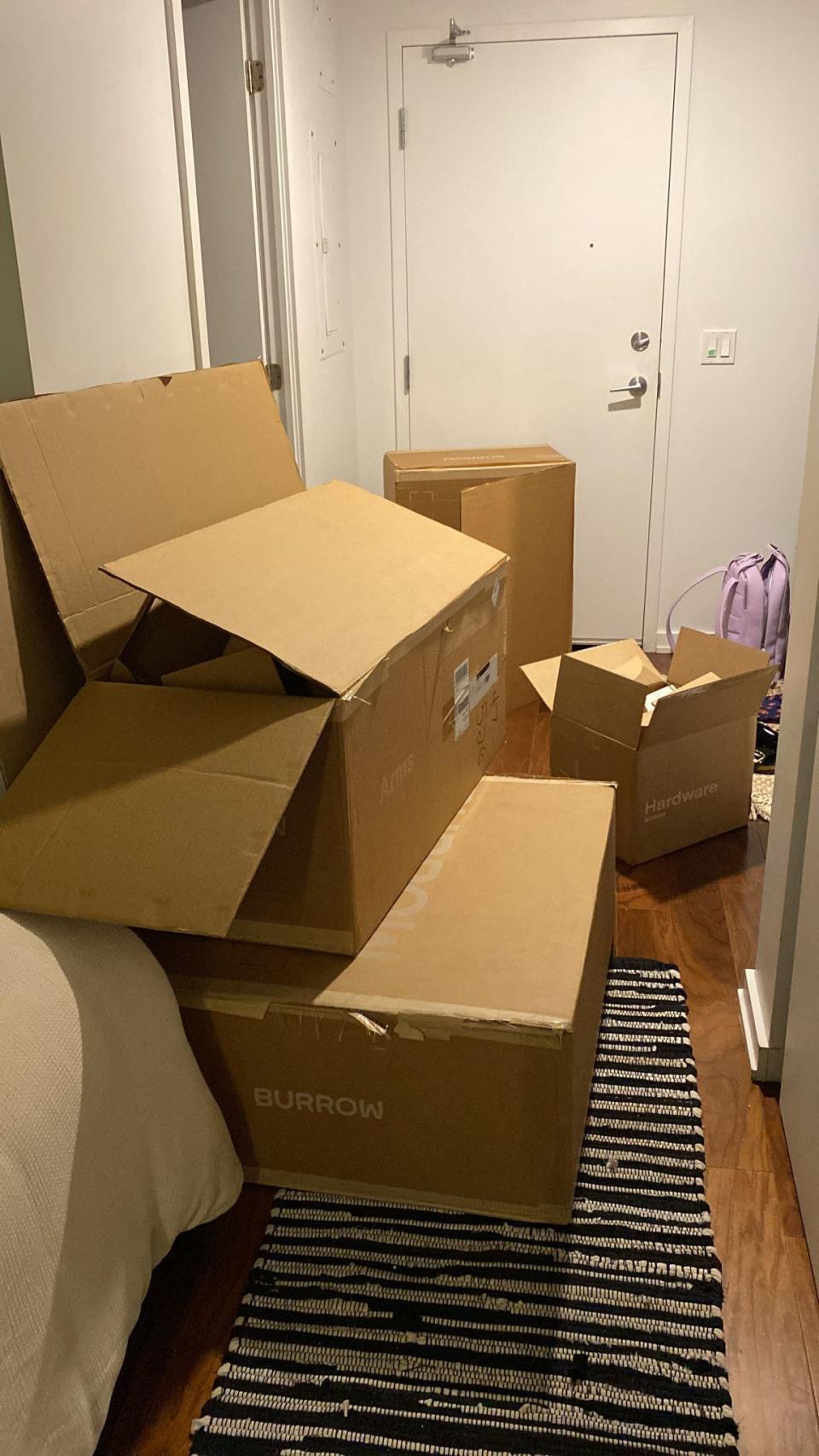 pile of open brown boxes sitting in hallway on black and white striped carpet, in front of door, burrow furniture delivery boxes