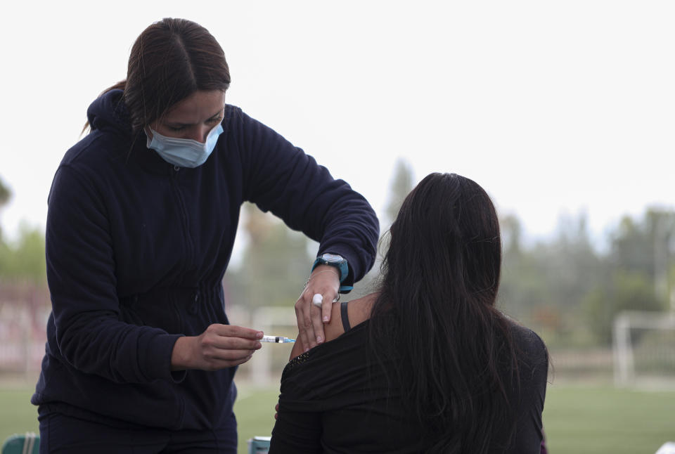 A healthcare worker injects a woman with a dose of the Sinovac COVID-19 vaccine at La Pintana Sports Complex turned into a makeshift vaccination site, in Santiago, Chile, Thursday, March 11, 2021, on the one-year anniversary that the World Health Organization declared the coronavirus a pandemic. (AP Photo/Esteban Felix)