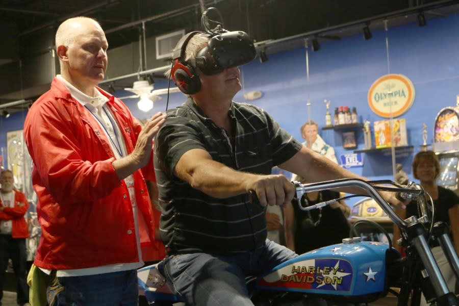 Jeff Handley, staff member at the Evel Knievel Musuem, helps visitor Kevin Diehl as he uses the virtual reality game to experience jumping over a group of police cars in Topeka, Kansas on June 21, 2017. (Photo credit should read BETH LIPOFF/AFP via Getty Images)