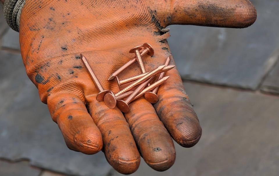 A glove is used when handling the copper nails used to fasten slate so that any visible nails will look the same as they age. Copper is used for its long life. The shingles on a good quality slate roof can last centuries.