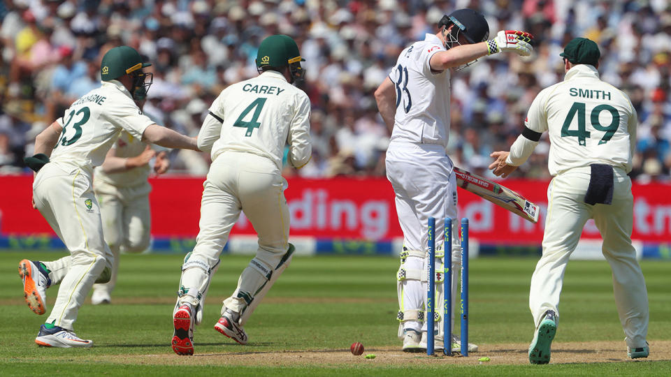 Harry Brook looks down at his stumps as Australian players celebrate his wicket around him.