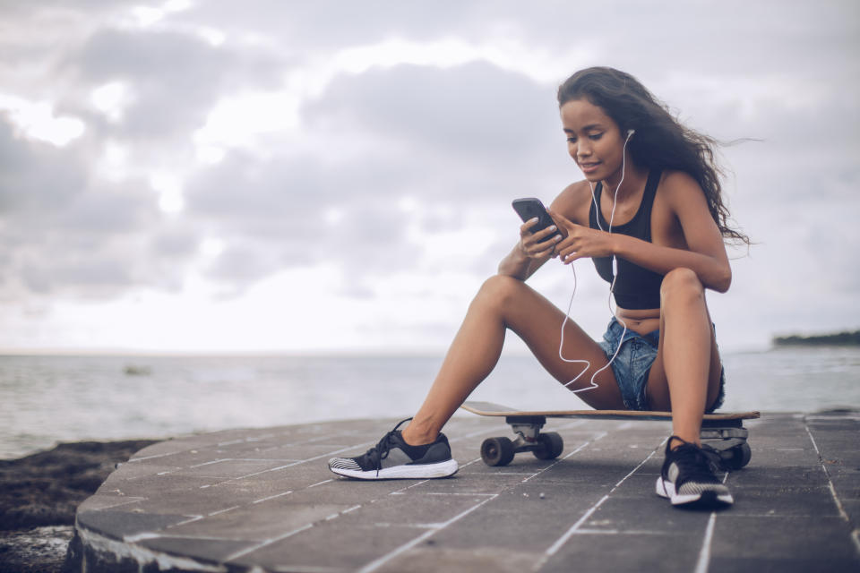 A woman sits on a skateboard looking at her phone.