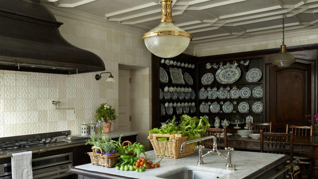 kitchen with square dark cast iron island with small sink and white marble top and oval light fixture overhead and a large old looking oven with a wide hood and the walls covered in a pale creamish yellow linen paper