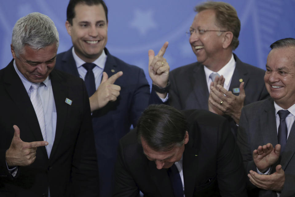 Lawmakers make finger-gun hand gestures as Brazil's President Jair Bolsonaro signs a second decree that eases gun restrictions, at Planalto presidential palace in Brasilia, Brazil, Tuesday, May 7, 2019. The decree opens Brazil’s market to guns and ammunition made outside of Brazil according to a summary of the decree. Gun owners can now buy between 1,000 -5,000 rounds of ammunition per year depending on their license, up from 50 rounds. Lower-ranking military members can now carry guns after 10 years of service. (AP Photo/Eraldo Peres)