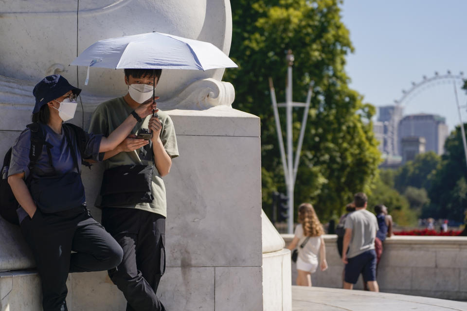 FILE - Tourists shelter from the sun under an umbrella as they stand on Queen Victoria Memorial, in London, Aug. 11, 2022. What's considered officially “dangerous heat” in coming decades will likely hit much of the world at least three times more often as climate change worsens, according to a new study. (AP Photo/Alberto Pezzali, File)