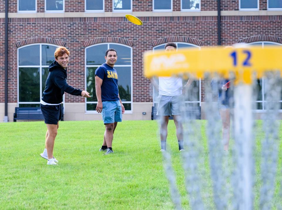 Brendan Robbins, left, a senior at Siena Heights University from New Boston, watches his disc fly toward a disc golf basket Friday on the SHU campus.