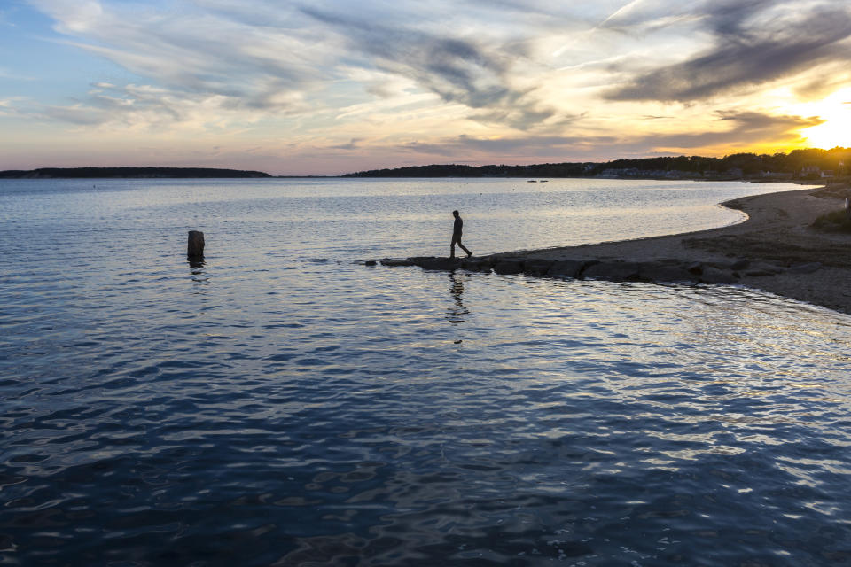 Man silhouetted walking on sandy point at Wellfleet Bay during sunset