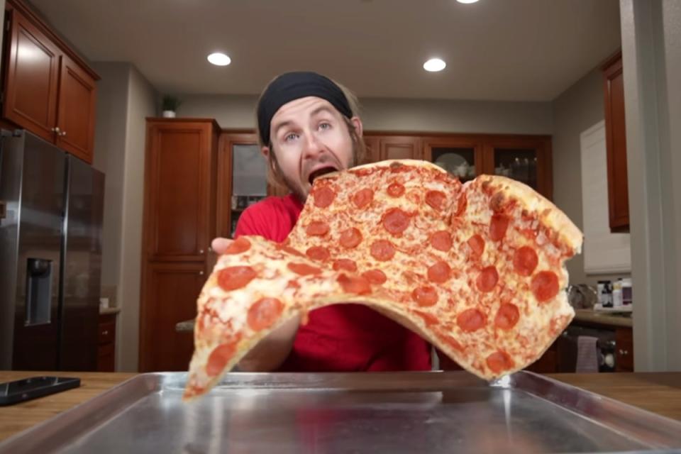 Fitness influencer Erik Lamkin munches into a giant slice of pizza on his YouTube channel (YouTube)