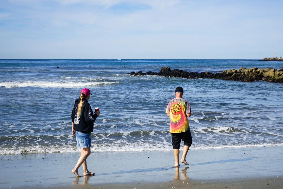 Couple walking barefoot on beach with coffee in hand in San Diego, California.