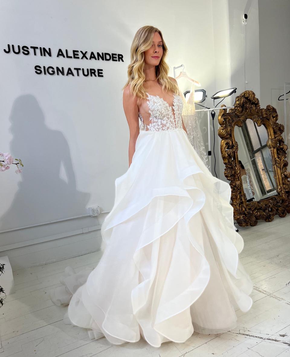 A woman poses in a wedding dress with cutouts on the sides and a tiered skirt.