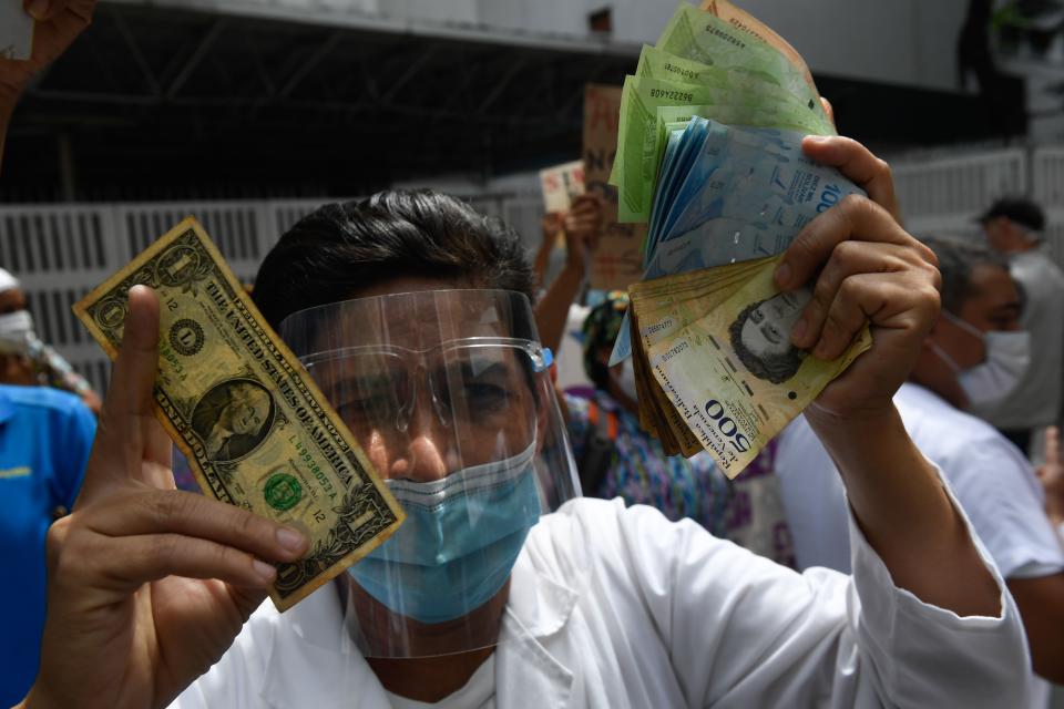 TOPSHOT - A health worker wearing a face mask and shield holds a one dollar bill in one hand and its equivalent in Bolivar bills -his salary- in the other, during a protest for the lack of medicines, medical supplies and poor conditions in hospitals, in Caracas on October 29, 2020, amid the new coronavirus pandemic. (Photo by Federico PARRA / AFP) (Photo by FEDERICO PARRA/AFP via Getty Images)