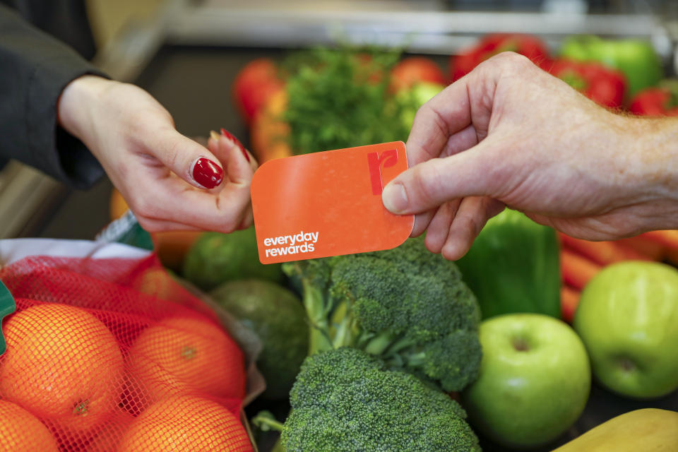 A man hands a woman a Woolworths Everyday Rewards card in front of fruit and vegetables. 