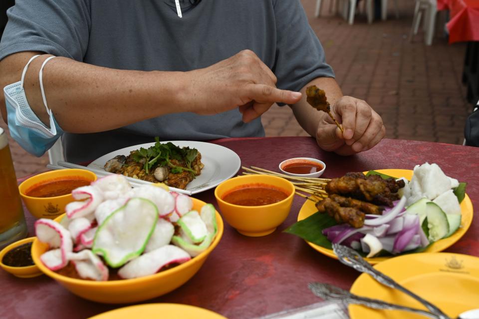 This photograph taken on January 13, 2021 shows KF Seetoh, founder of Makansutra, gesturing at a stick of satay at the Makansutra Gluttons Bay hawker food centre in Singapore. - A small but growing number of young Singaporean street food vendors, or "hawkers", are fuelling hopes that a new generation will preserve the city-state's culinary traditions.