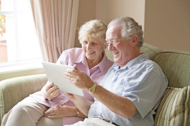 Elderly couple, aged 75-80, looking at photos on a tablet computer in a private retirement home