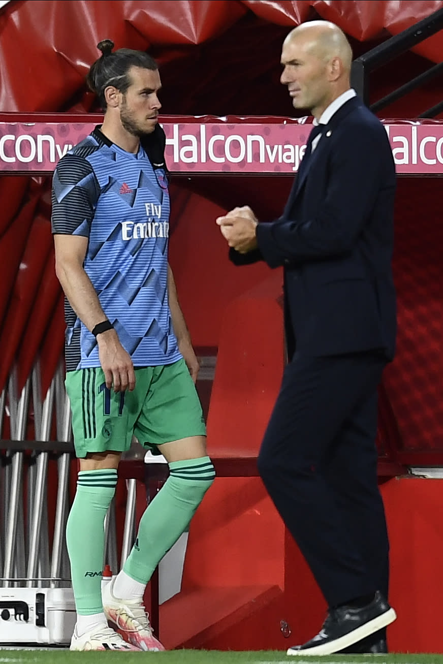 Real Madrid's head coach Zinedine Zidane, right, talks with Real Madrid's Gareth Bale during the Spanish La Liga soccer match between Granada and Real Madrid at the Los Carmenes stadium in Granada, Spain, Monday, July 13, 2020. (AP Photo/Jose Breton)