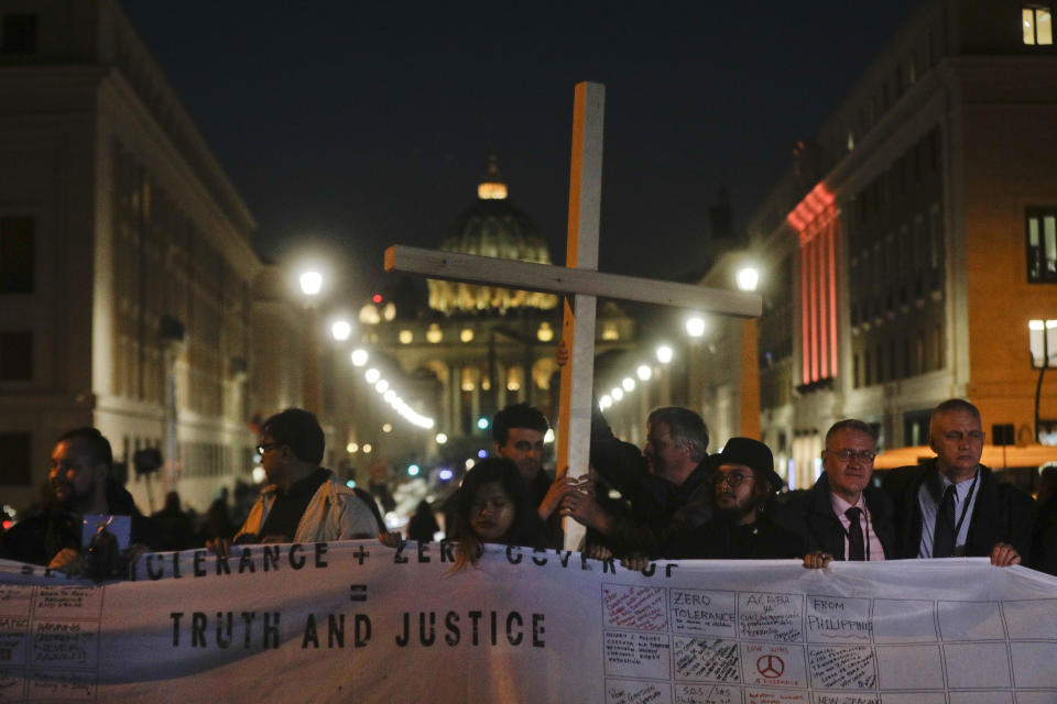 FILE - Survivors of sex abuse hold a cross as they gather in front of Via della Conciliazione, the road leading to St. Peter's Square, visible in background, during a twilight vigil prayer of the victims of sex abuse, in Rome, Thursday, Feb. 21, 2019. Five years ago this week, Francis convened an unprecedented summit of bishops from around the world to impress on them that clergy abuse was a global problem and they needed to address it, but now, five years later, despite new church laws to hold bishops accountable and promises to do better, the Catholic Church's in-house legal system and pastoral response to victims has proven again to be incapable of dealing with the problem. (AP Photo/Gregorio Borgia, file)