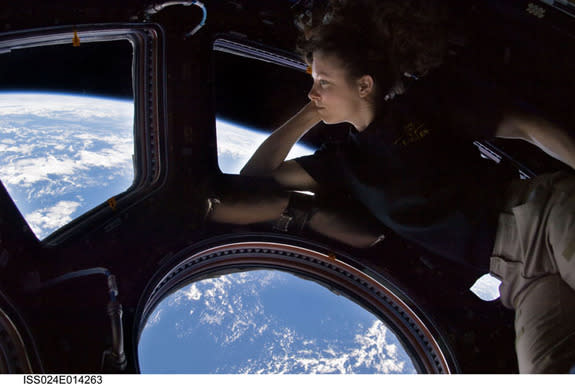 NASA astronaut Tracy Caldwell Dyson, Expedition 24 flight engineer, looks through a window in the Cupola of the International Space Station. A blue and white part of Earth and the blackness of space are visible through the windows. The image wa