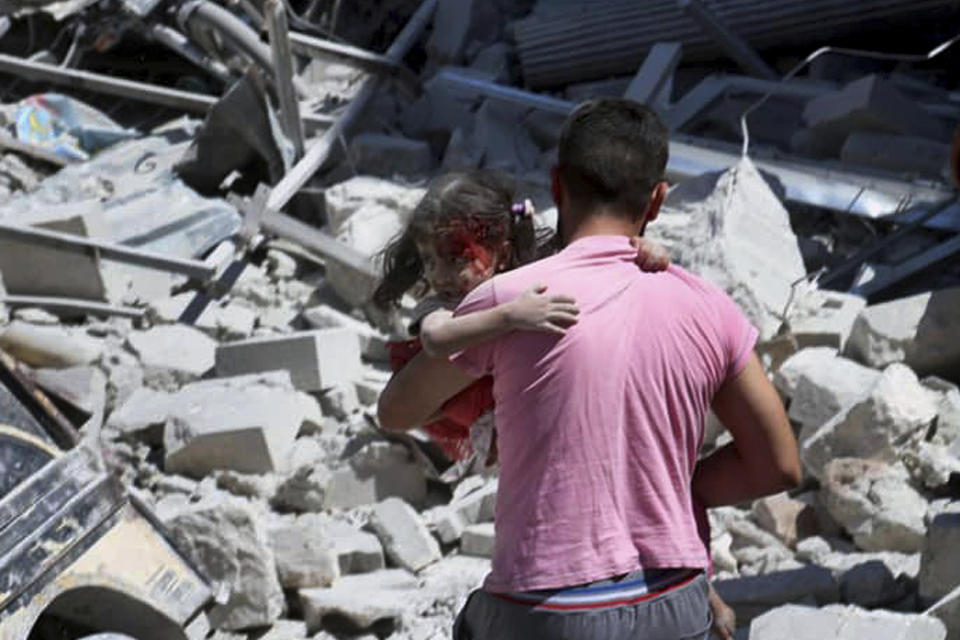 This photo provided by the Syrian Civil Defense White Helmets, which has been authenticated based on its contents and other AP reporting, shows a Syrian man carrying an injured girl after an airstrike hit the northern town of Ariha, in Idlib province, Syria, Saturday, July 27, 2019. Syrian activists and a doctor say a government airstrike killed several people when it hit a weekly open-air market in a busy town in the last rebel stronghold in northwestern Syria. (Syrian Civil Defense White Helmets via AP)