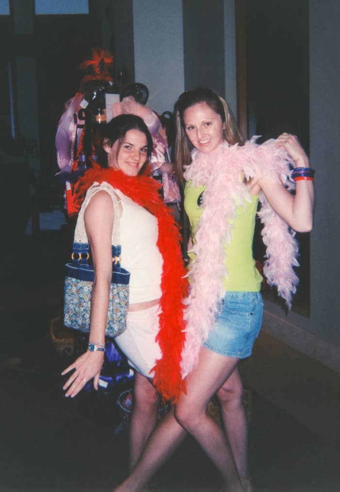 Two women pose happily, smiling and wearing feather boas; one in red and the other in pink. They appear to be enjoying a fun, casual event. Names unknown