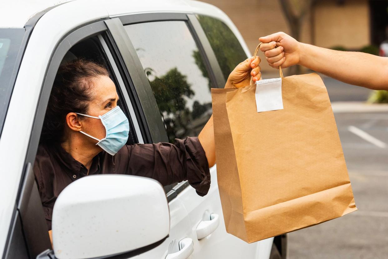 Women in her car being handed her curbside pickup shopping bag.