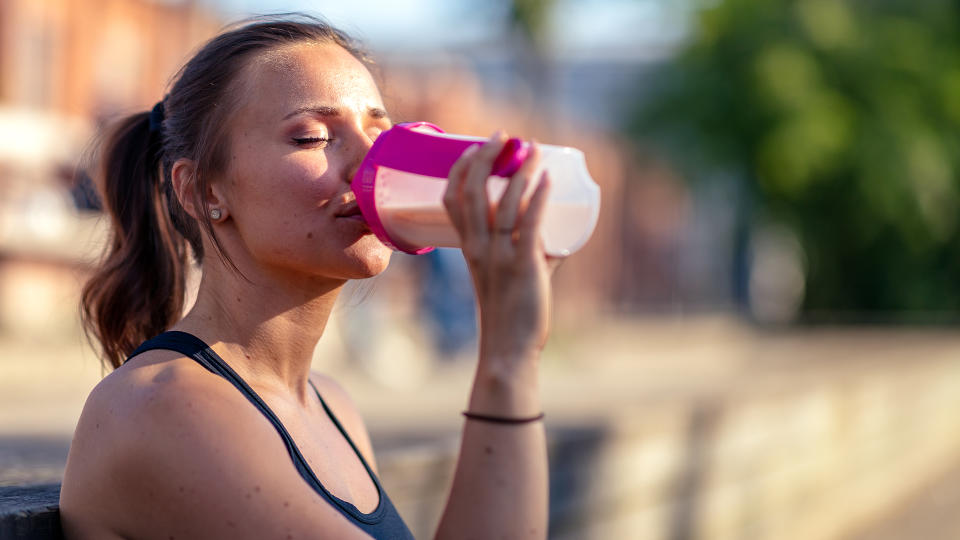 A woman drinking a recovery shake from a flask