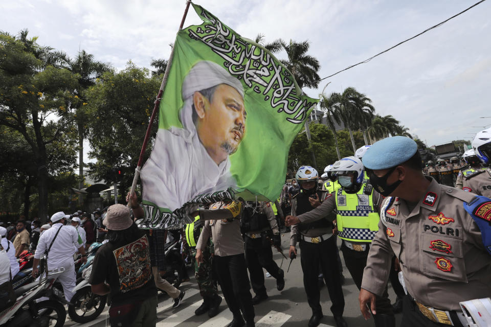 Supporters of Rizieq Shihab, leader of the Islam Defenders Front, display a flag bearing his image during a rally in Jakarta, Indonesia, Friday, Dec. 18, 2020. Hundreds of protesters marched in Indonesia's capital on Friday to demand the release of the firebrand cleric who is in police custody on accusation of inciting people to breach pandemic restrictions and ignoring measures to curb the spread of COVID-19 by holding several events, and justice for his six followers who were killed in a shootout with the police. (AP Photo/Tatan Syuflana)