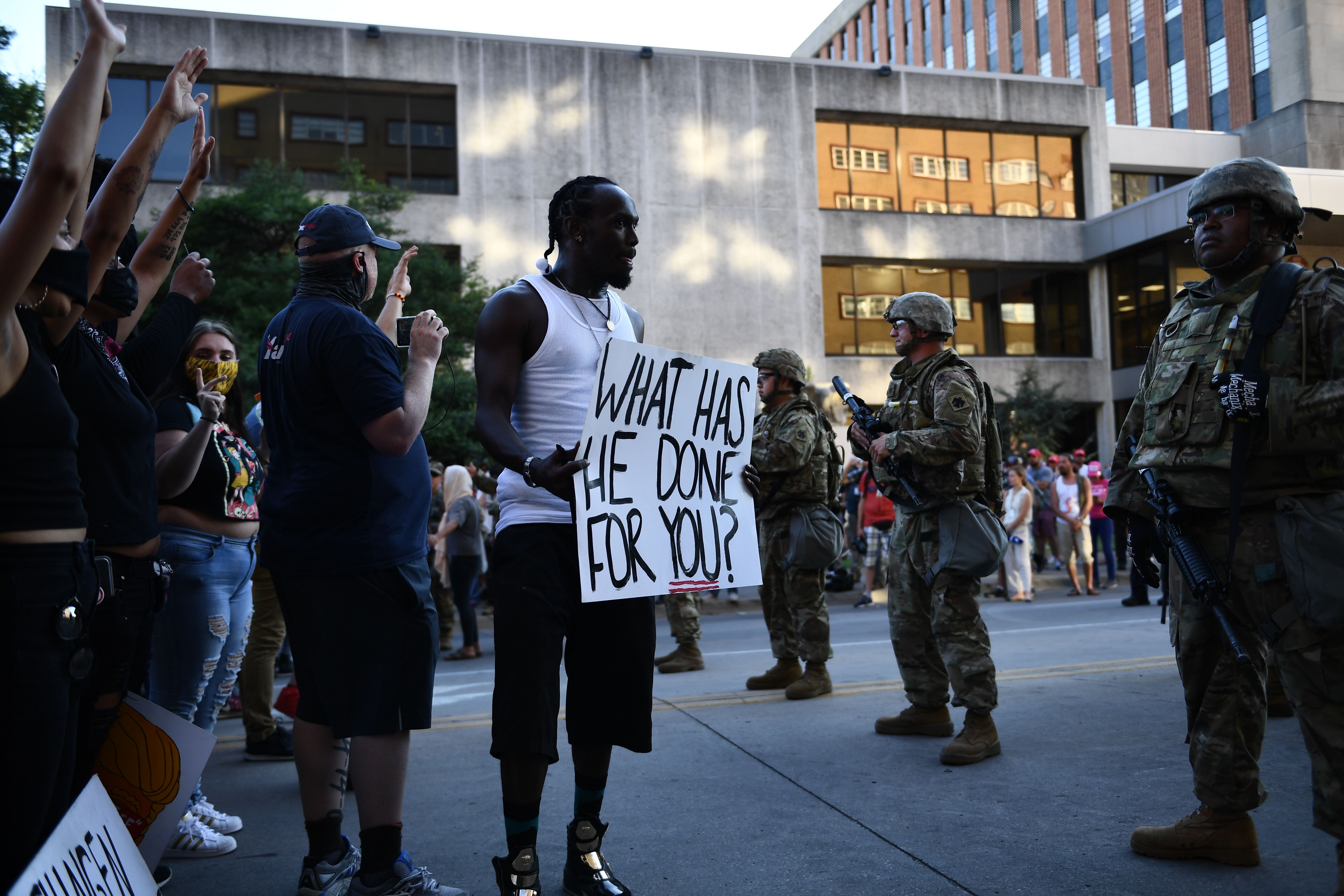Delano Frazir a "Black Lives Matter" protestor holds a sign in front of National Guards in Tulsa, Oklahoma where Donald Trump holds a campaign rally at the BOK Center on June 20, 2020. - Hundreds of supporters lined up early for Donald Trump's first political rally in months, saying the risk of contracting COVID-19 in a big, packed arena would not keep them from hearing the president's campaign message. (Photo by Brendan Smialowski / AFP) (Photo by BRENDAN SMIALOWSKI/AFP via Getty Images)