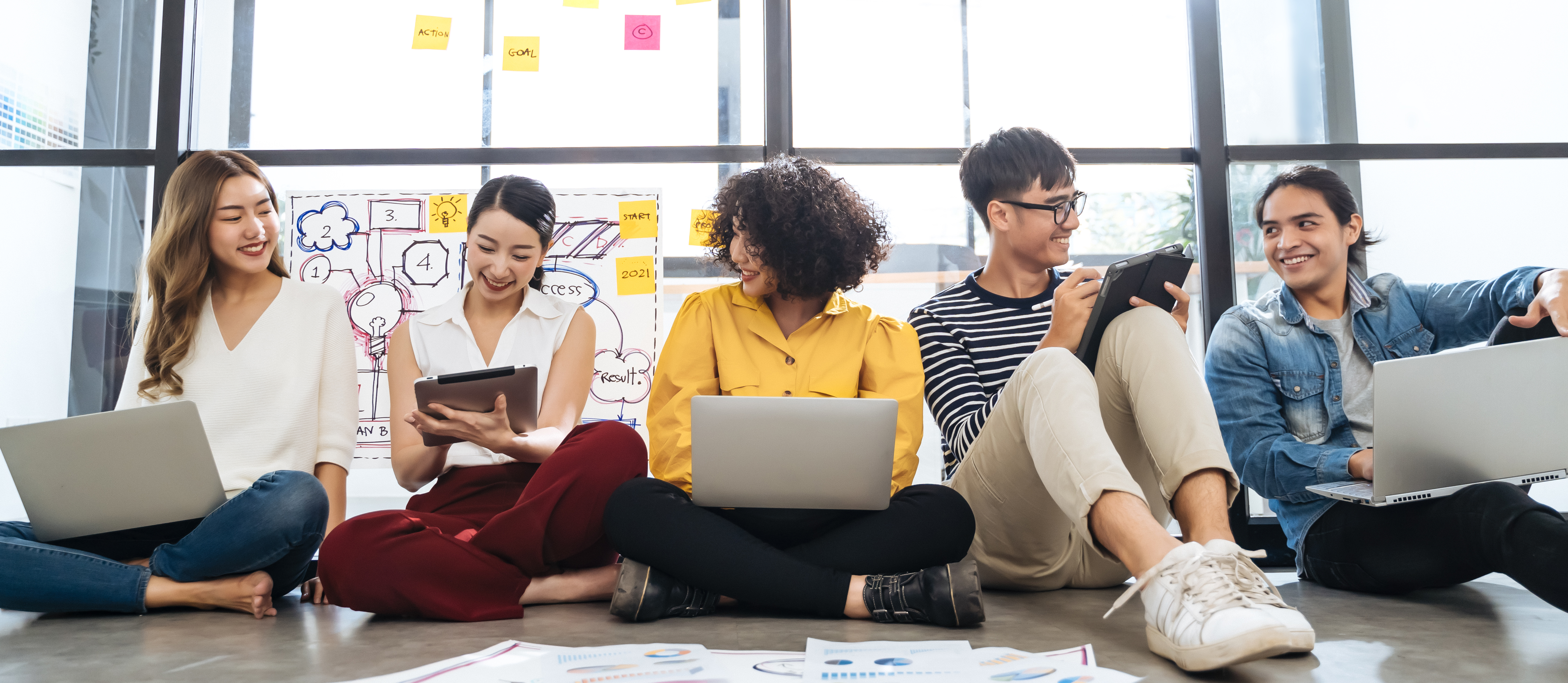 Group of young happy Asian creative business people or hipster student using electronic devices tablet and laptop connection together in modern office. Creative lifestyle young people concept