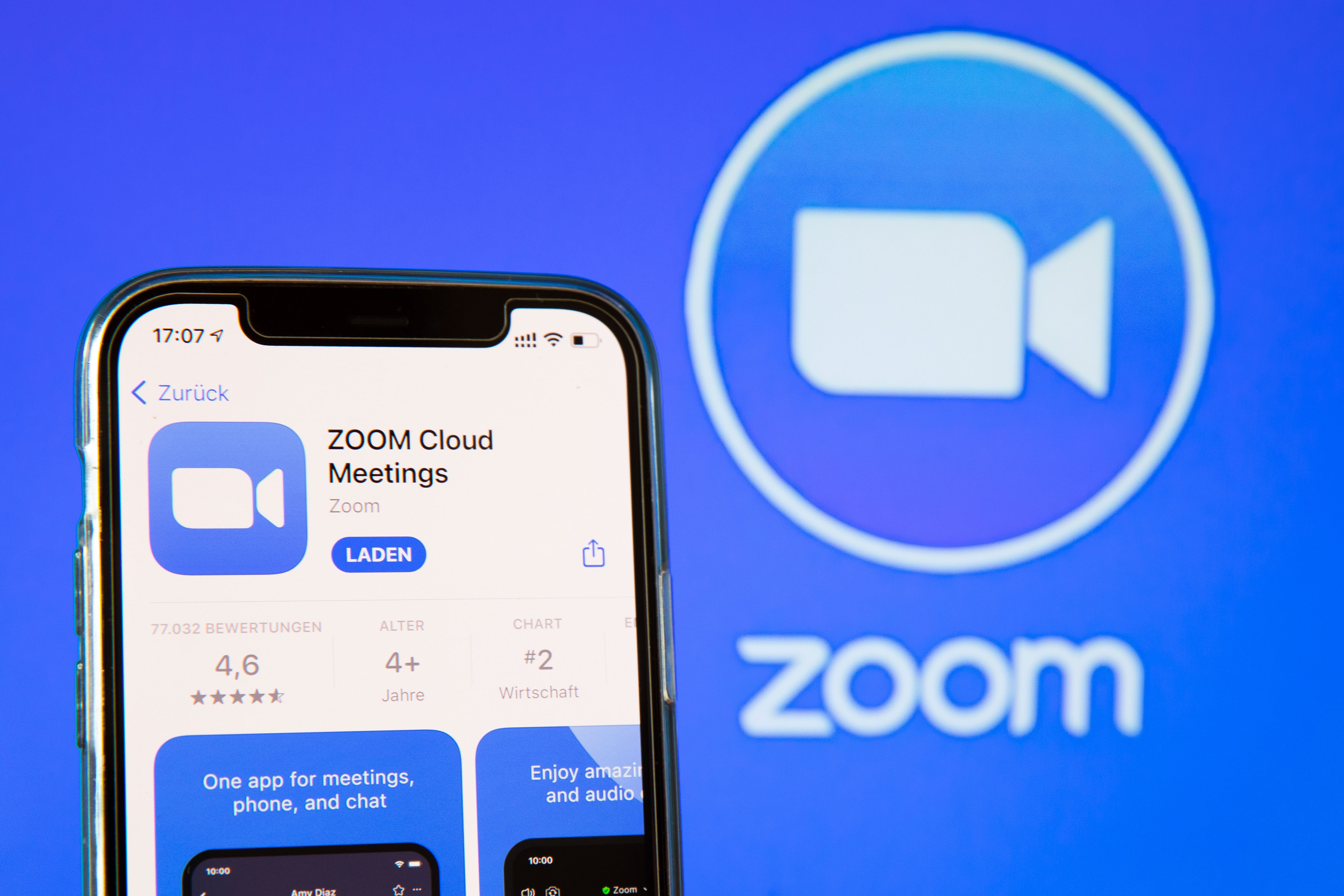  The image shows a search result for the Zoom Cloud Meetings app on a mobile phone with a Zoom logo in the background.