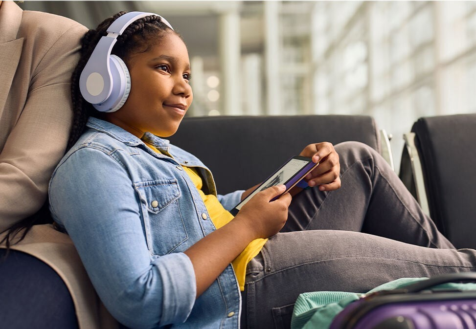 A child wearing headphones listens to an audiobook using a Kindle Paperwhite Kids e-reader,