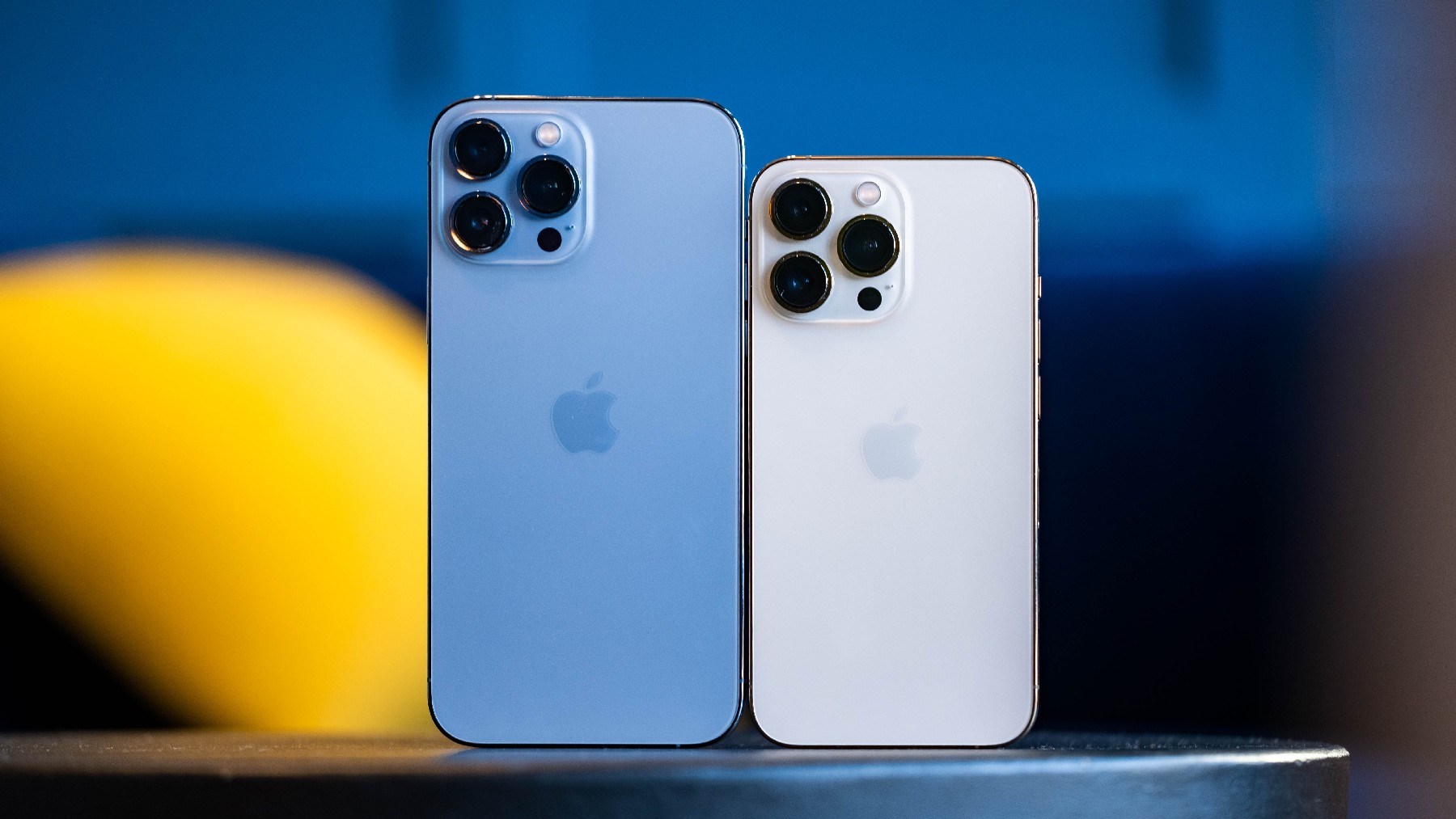 A blue iPhone 13 Pro Mac and a gold iPhone 13 Pro next to each other on a table with their rear cameras facing us." data-uuid="b123ee1c-4c03-3fed-800e-fe42028b6791