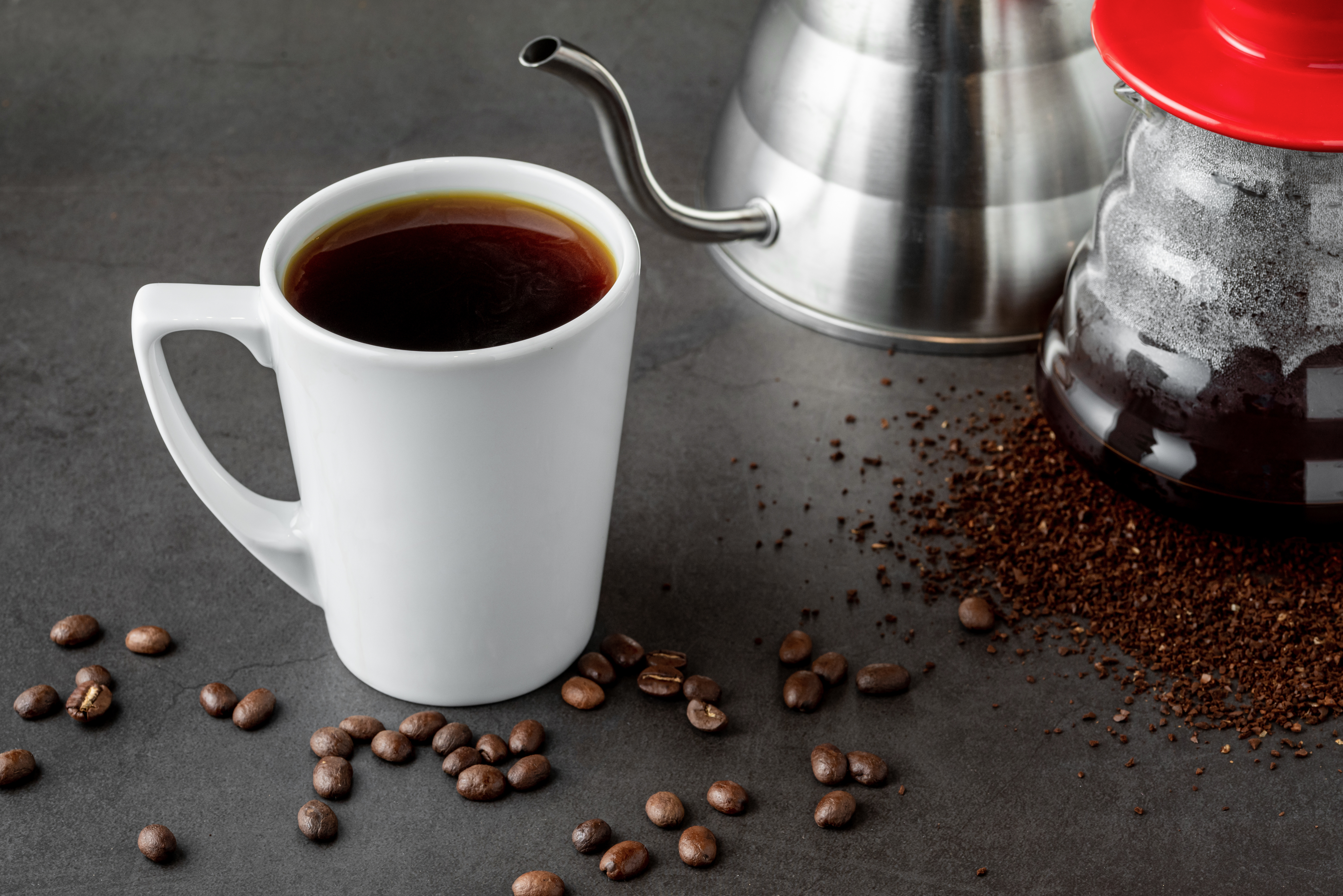 A cup of coffee and third generation pour over coffee brewing equipment on stone floor