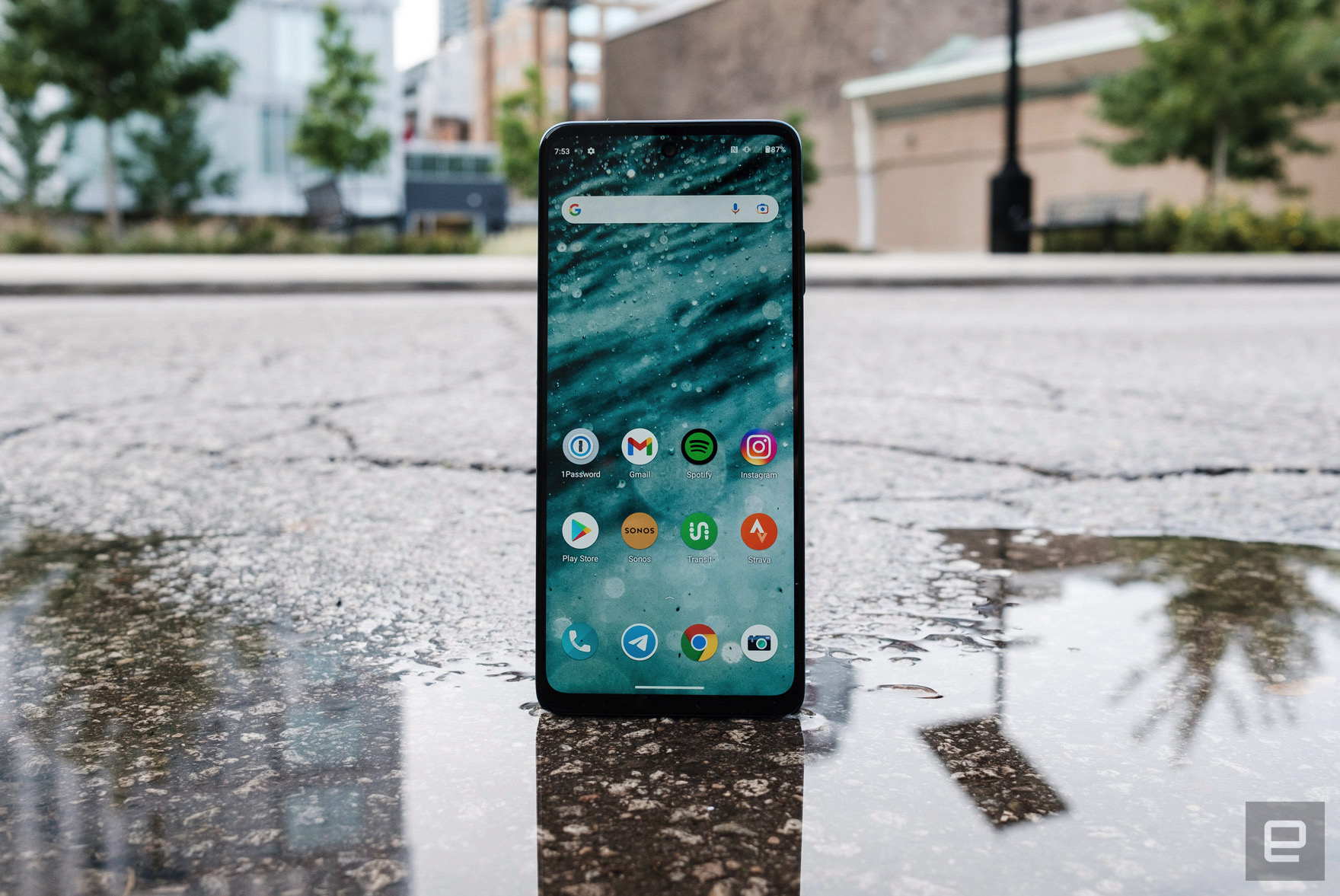 The Motorola Moto Edge photographed in the street standing up on the edge of a puddle with its reflection visible in the foreground.