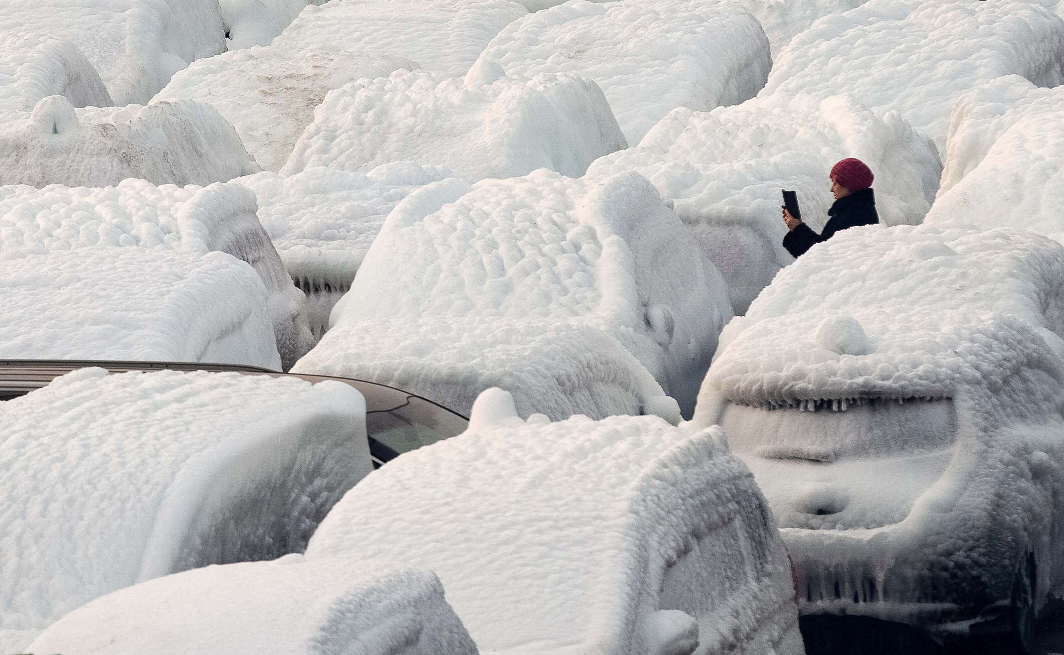 A woman takes a picture of ice-covered vehicles unloaded from the cargo ship Sun Rio, which was caught in severe weather conditions in the Sea of Japan, in the port of Vladivostok, Russia December 29, 2021. REUTERS/Tatiana Meel     TPX IMAGES OF THE DAY