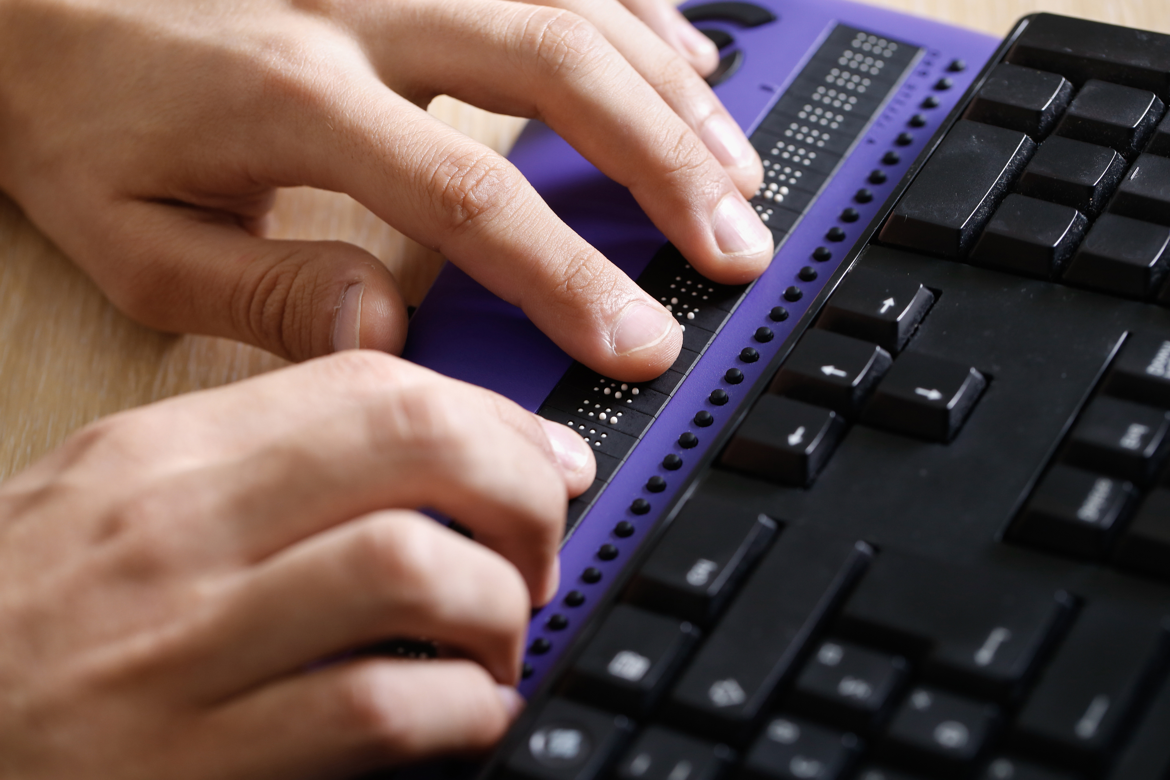 Blind person using computer with braille computer display and a computer keyboard. Blindness aid, visual impairment, independent life concept.