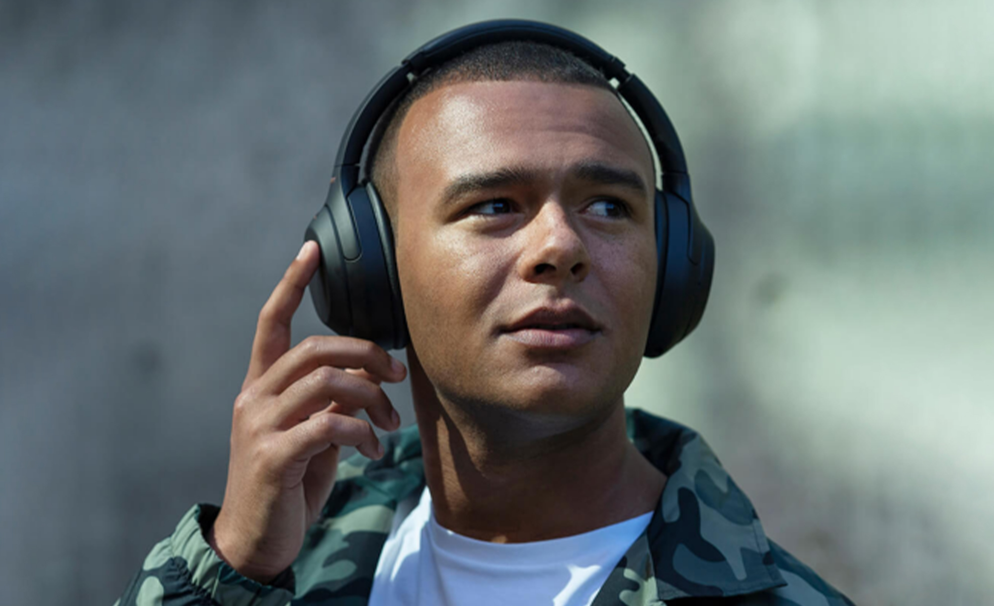 A man in a camoflague jacket wearing black Sony WH-1000XM4 headphones.