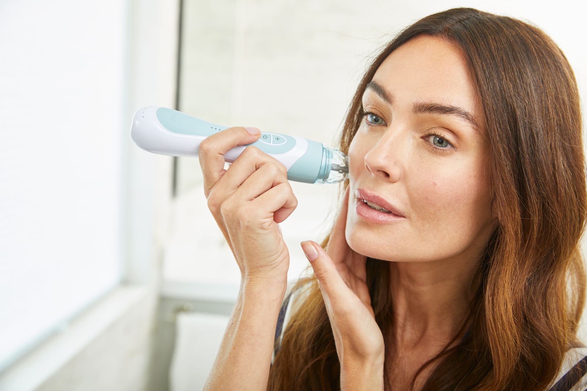 A person holding a light blue PMD Personal microdermabrasion device to their face with one hand while pulling their skin taut with the other.