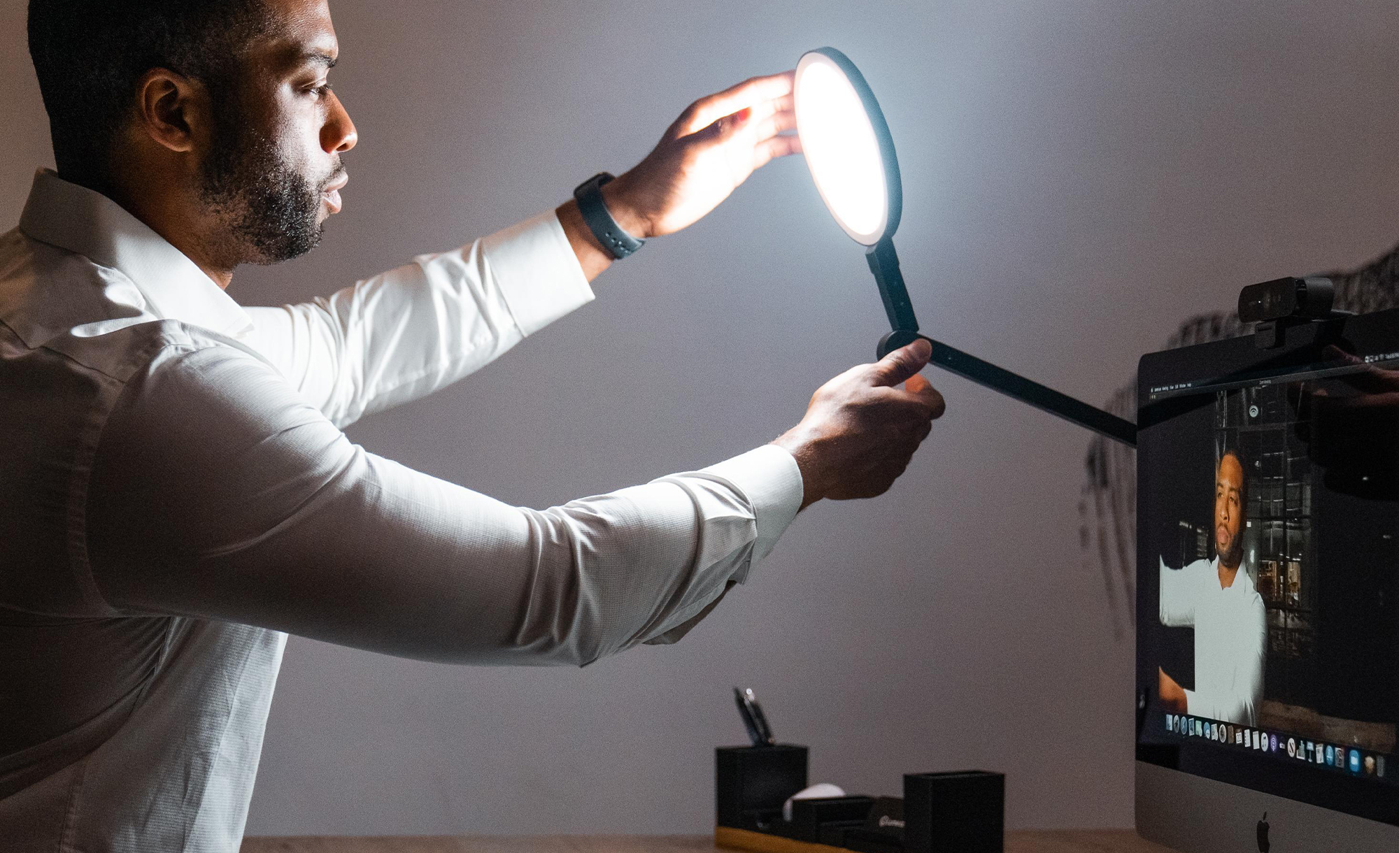 A man adjusting the position of the LumeCube Edge lamp next to a computer monitor.