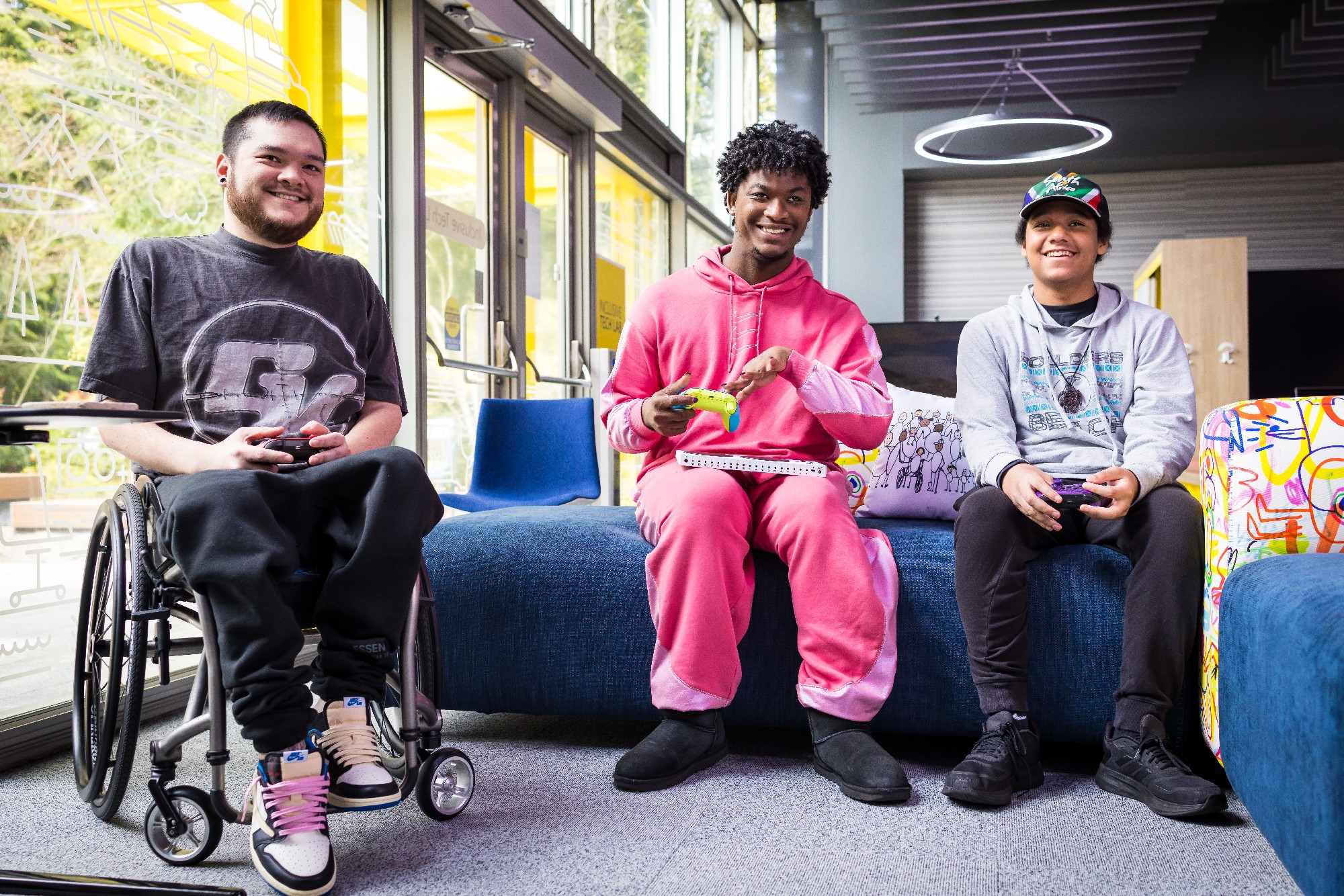 Three people inside the gaming section of Microsoft's new Inclusive Tech Lab. One of them is using a wheelchair, and all three are using Xbox controllers.