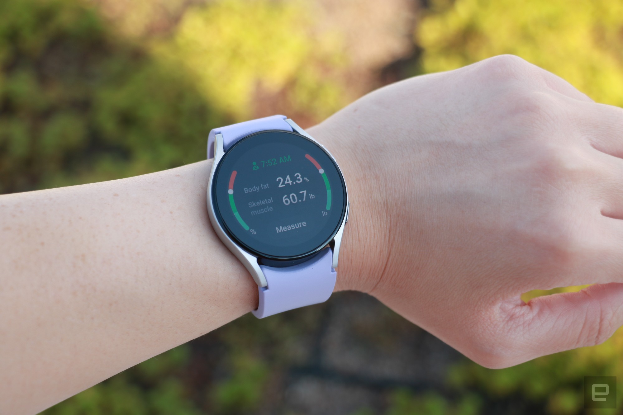 The Samsung Galaxy Watch 5 on a wrist, showing the device's body composition tool with some results displayed. The screen says Body fat is 24.3 percent, while Skeletal Muscle is 60.7 percent. A button at the bottom says 