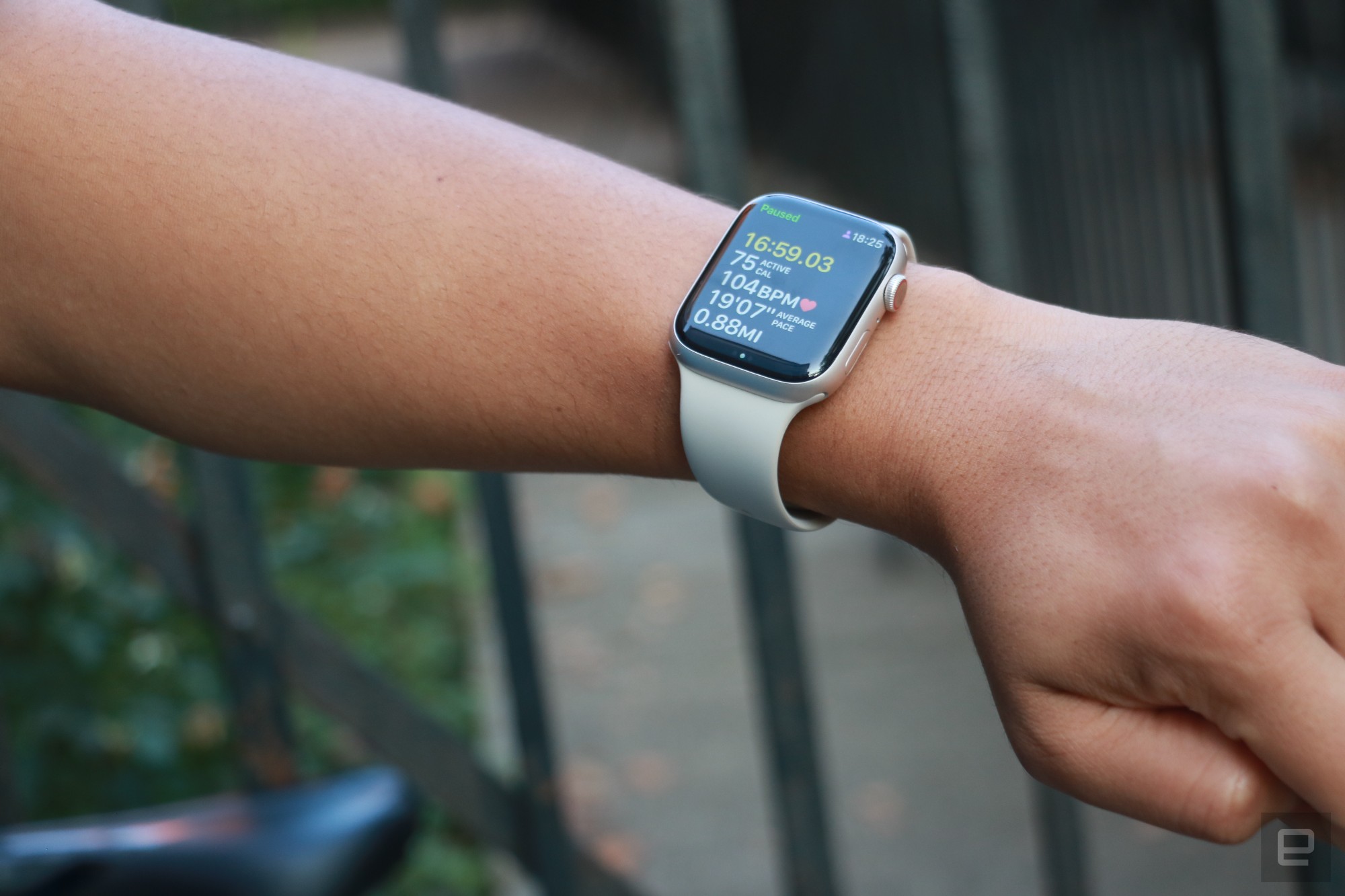 The Apple Watch Series 8 on the wrist of an arm held up in mid-air with a bike seat in the background.