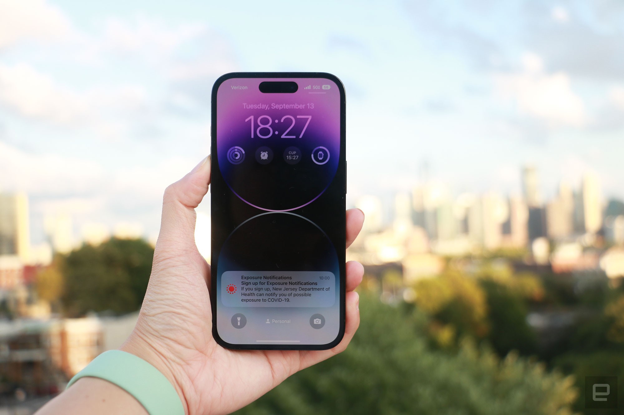 An iPhone 14 Pro held in mid-air against the New York skyline at sunset.