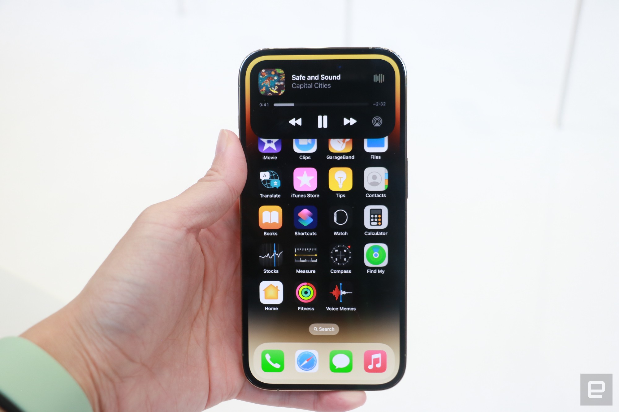 The iPhone 14 Pro held against a white background, with the new dynamic island cutout showing an Apple Music playback box." data-uuid="e2faca1f-b844-3fb8-8f88-5cd9cb7fc359