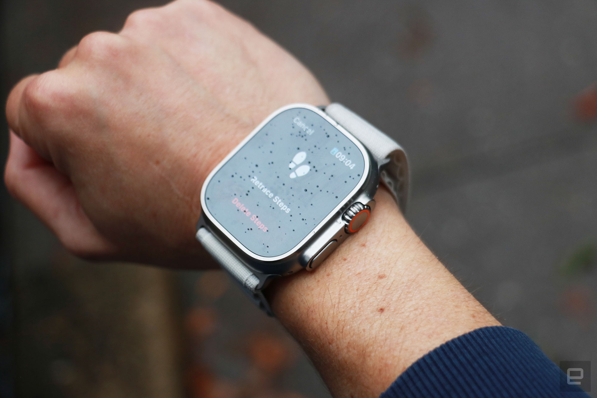 The Apple Watch Ultra, with drops of rain on its screen, on a person's wrist. The display shows the Backtrack feature, with a pair of footsteps up top and the options to 