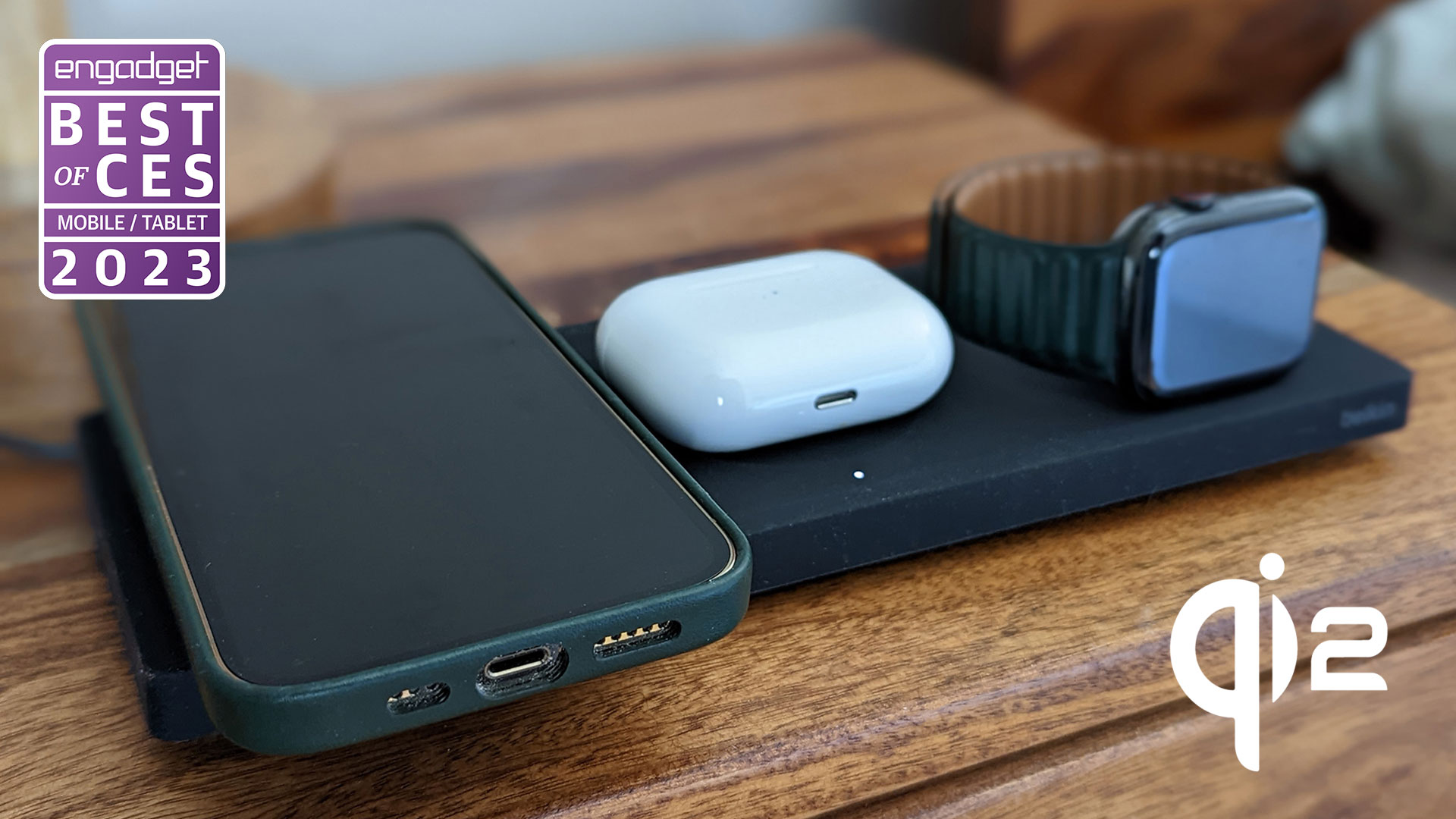 A Belkin wireless charger with a phone, AirPods case and Apple Watch charging on it sits on a wooden side table." data-uuid="5797a714-c0db-3d2c-9b97-3b239e857f32