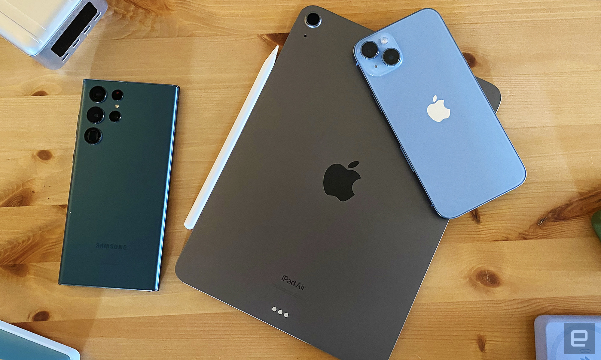 Overhead view of the devices used for battery testing arranged on a table, including an iPhone, Galaxy phone and iPad, all face down. 