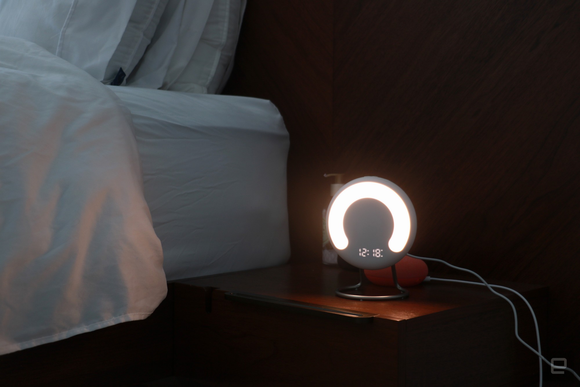 The Amazon Halo Rise on a nightstand in the dark with a the time and a semi-circle lit up on its front.